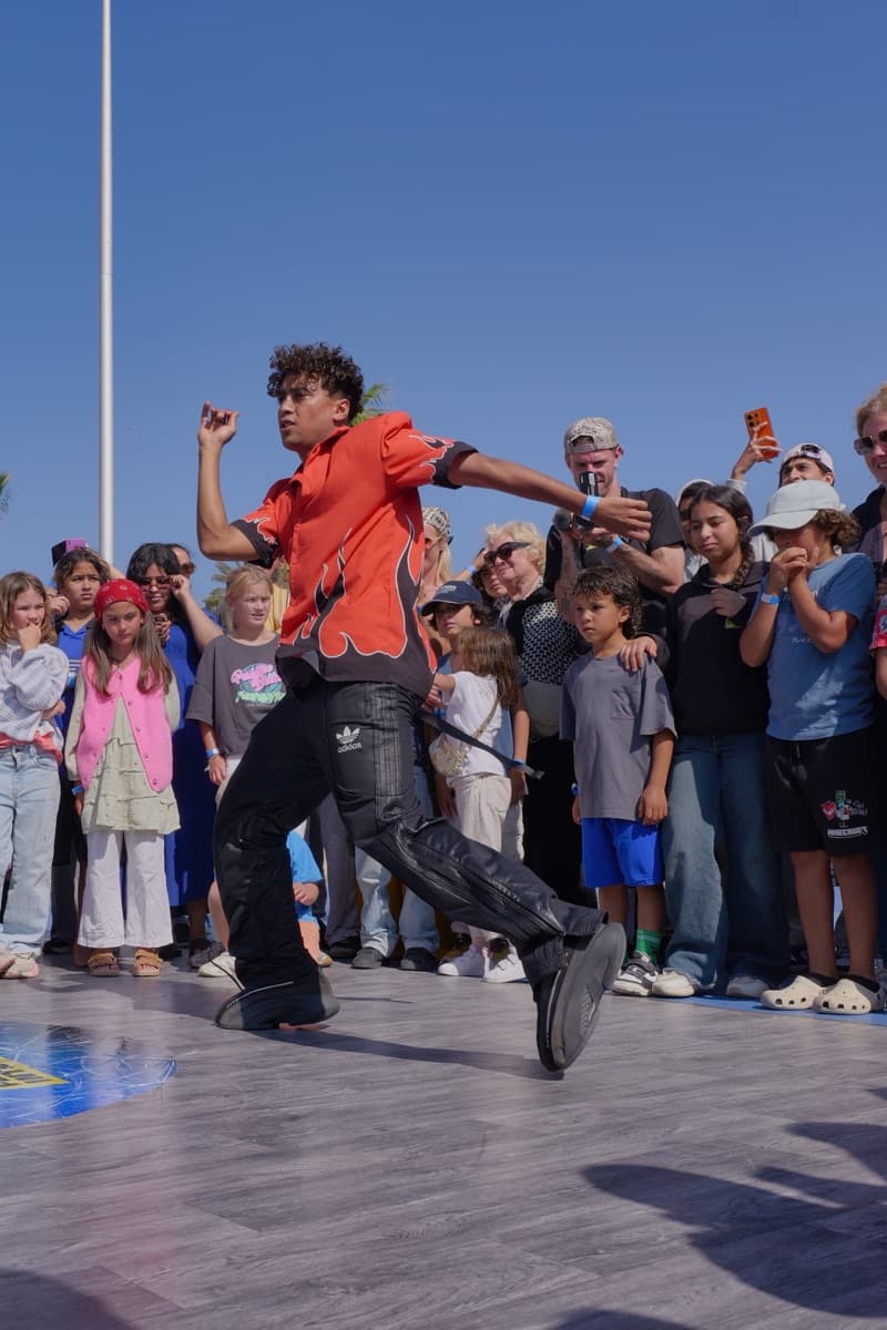 Un danseur en chemise rouge danse debout au centre du cercle, devant les enfants de la jam, sur la corniche d'Essaouira.