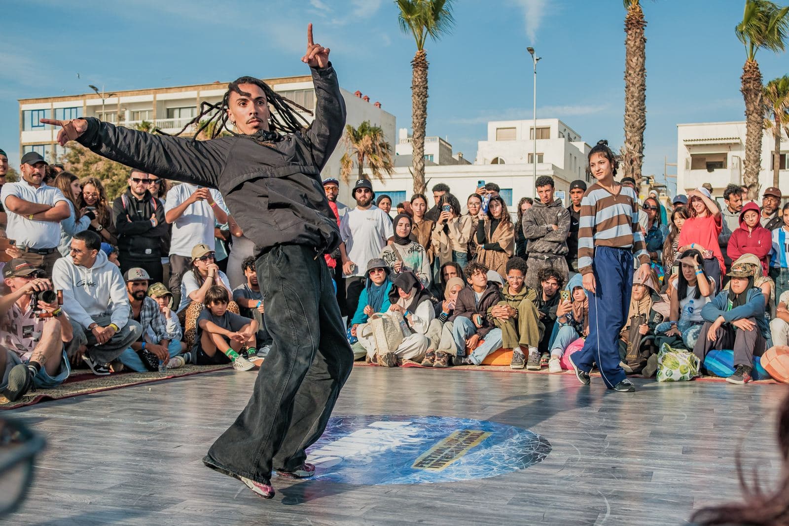 Un danseur aux longues tresses danse debout devant le public.